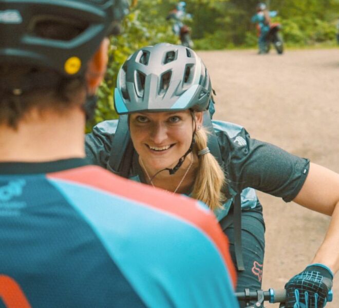 A rider smiling at their coach while practicing their mountain bike skills