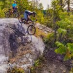 A client riding their mountain bike down a large rock obstacle during a skills camp