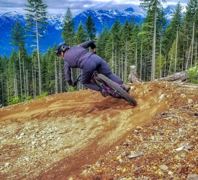A rider entering a left handed corner with a beautiful mountain and forest backdrop from the top of Squamish