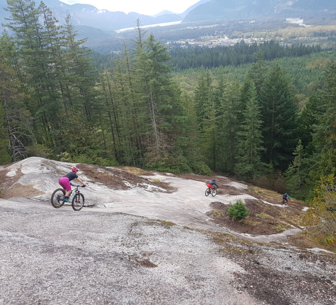 Three riders are riding down the giant slab on the trail In and Out Burger in Squamish