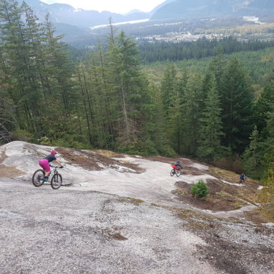 Three riders are riding down the giant slab on the trail In and Out Burger in Squamish