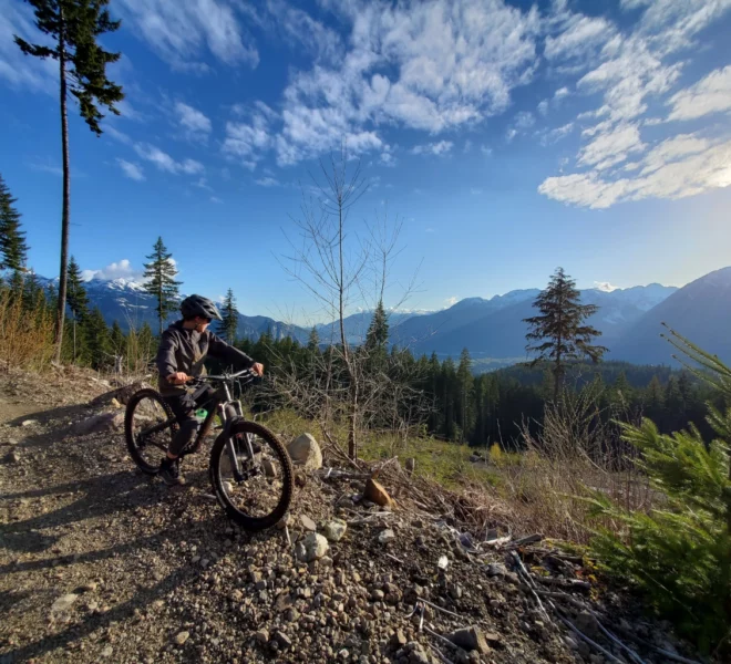 A solo rider at the top of the mountain biking trails taking in the view of the forest and mountains of Squamish