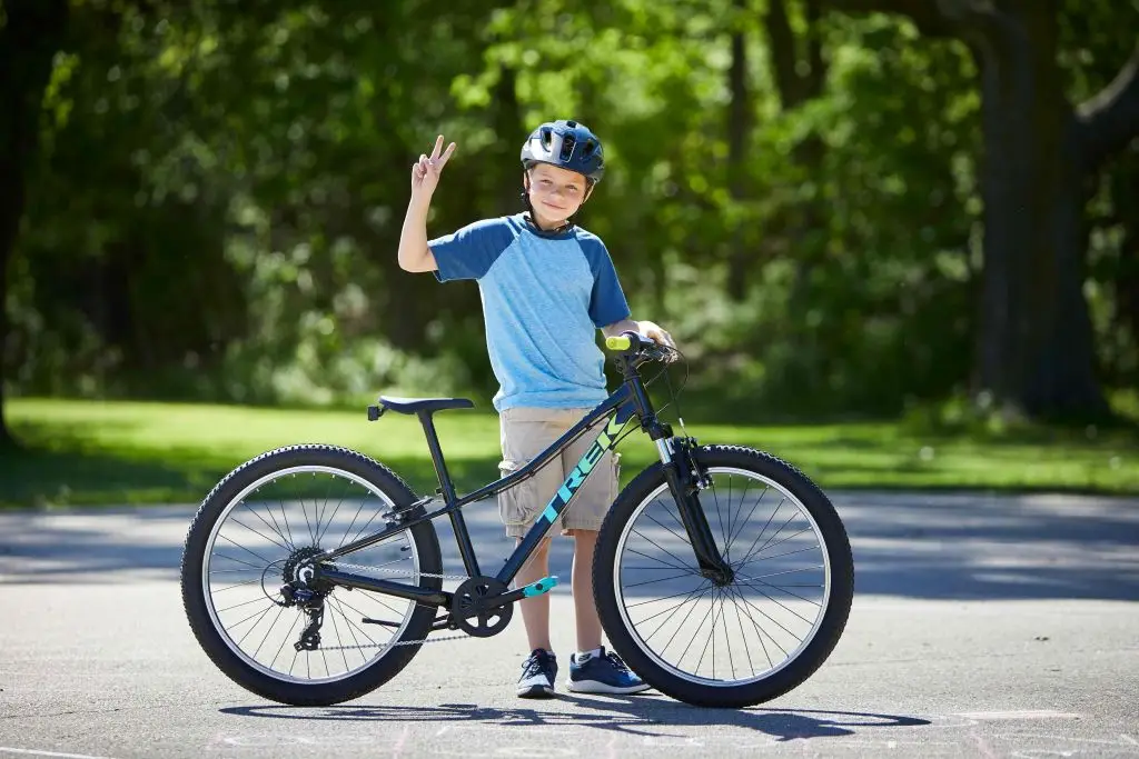 A boy is standing next to a bike and giving a thumbs up.