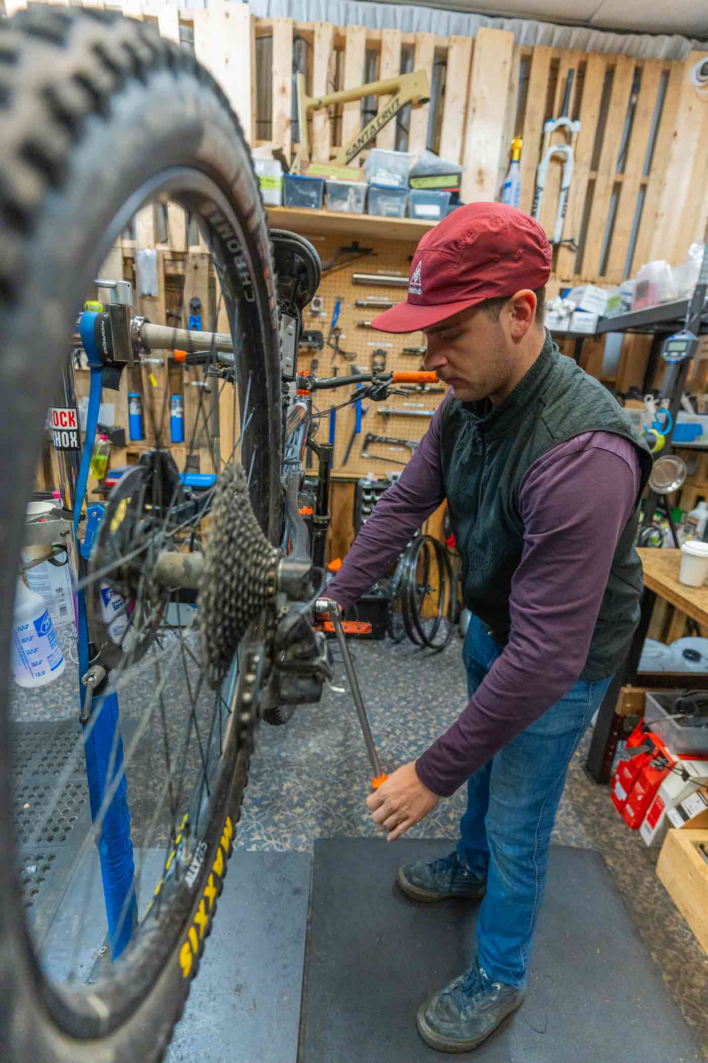 In a workshop in Squamish, British Columbia, a mechanic wearing a red cap is busy repairing a bicycle, surrounded by essential tools and equipment neatly arranged in the background.